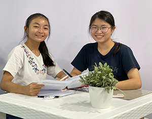 Two girls studying together on a desk with a potted plant in front of them