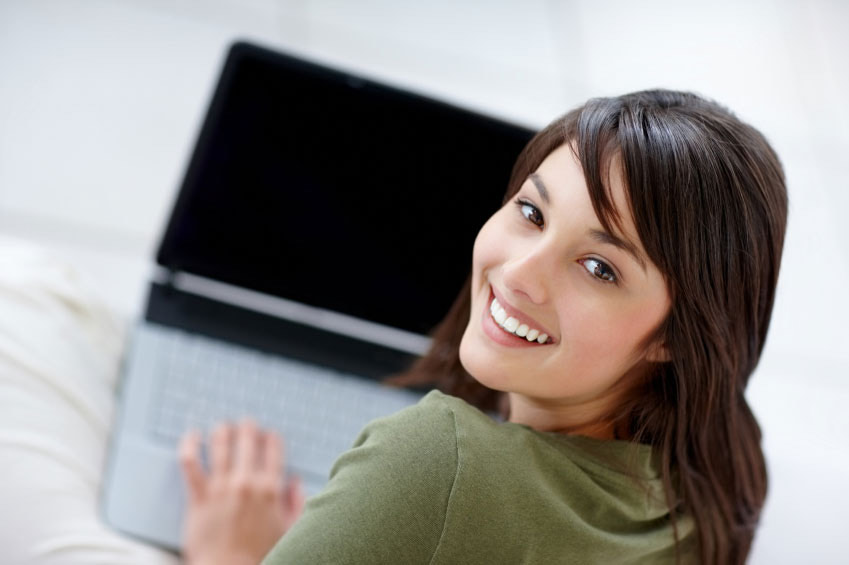A woman smiling while facing the camera, hand resting on a laptop