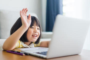 A girl in front of a laptop with her right hand raised